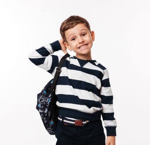 Portrait of a confused cute little kid with backpack scratching his head and looking at camera isolated over white background